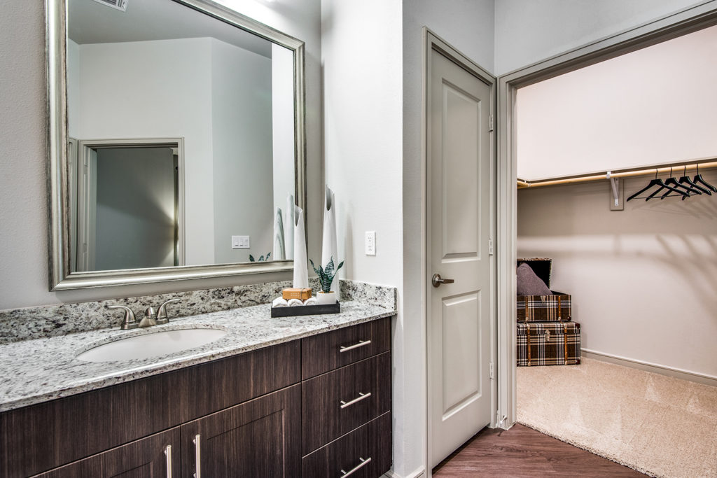 Model apartment bathroom with single vanity, linen closet, and large walk-in closet