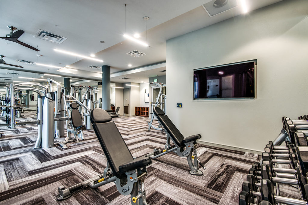 Strength training machines and free weights in community fitness center with wall-mounted TVs